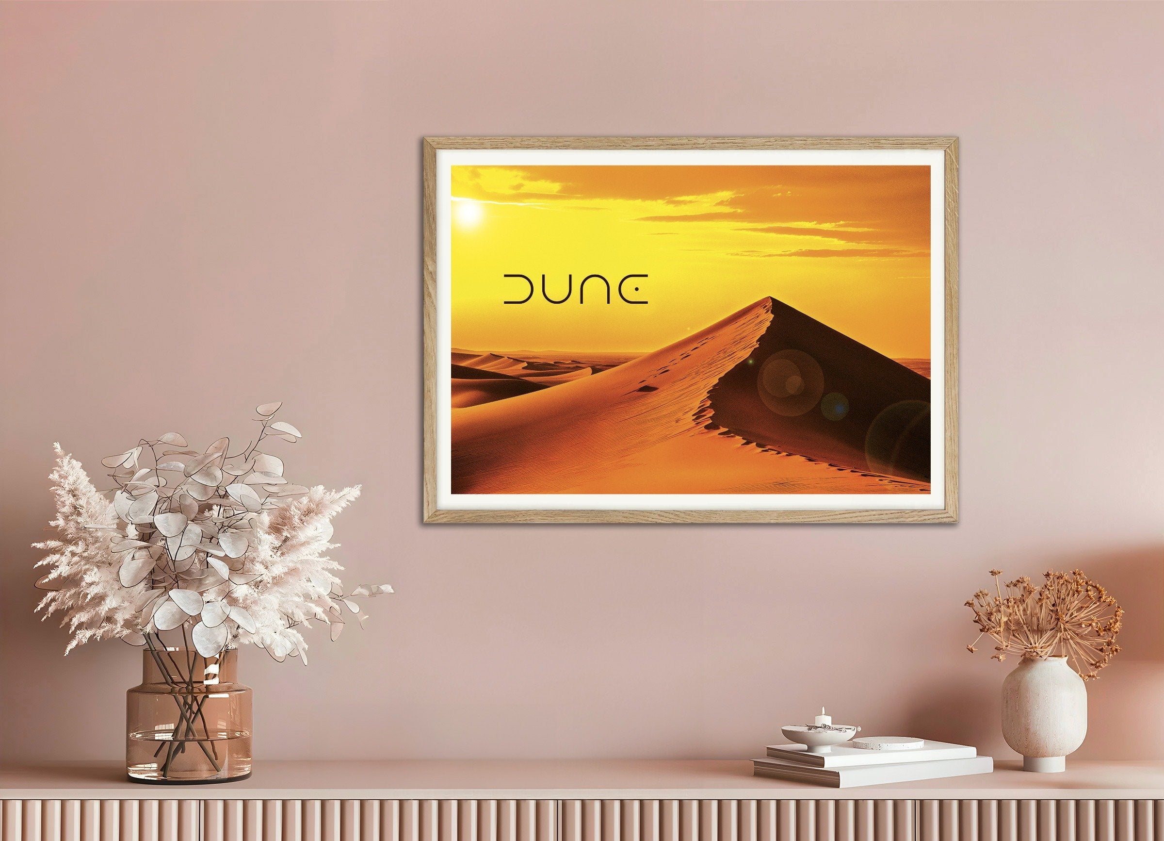 Framed 'Dune' poster on a pink wall with decorative items below.