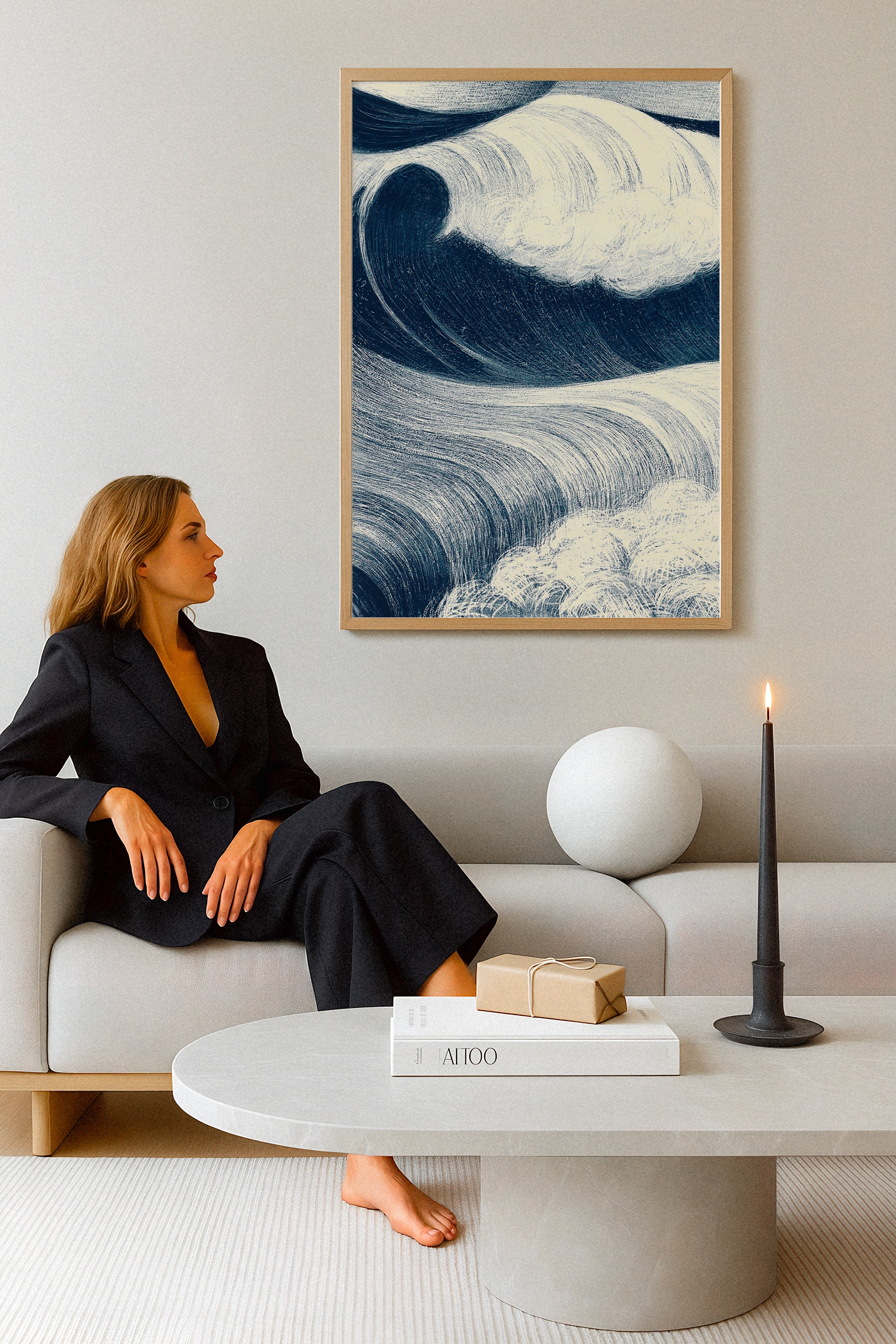 Affiche artistique de vagues bleues encadrée et accrochée dans un salon moderne et épuré, avec une femme élégante assise sur un canapé beige, une table basse en pierre et une bougie noire allumée.